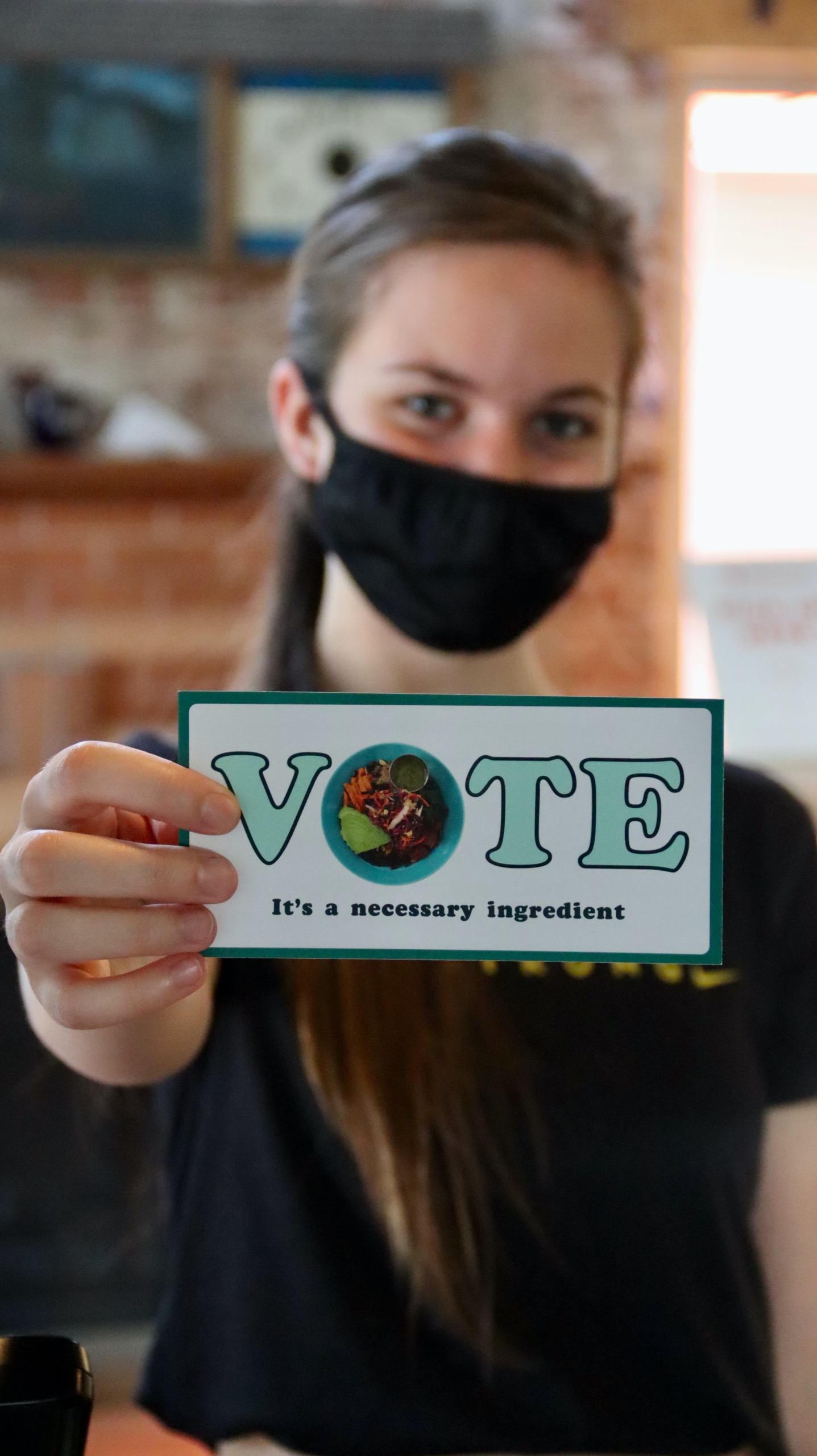 VOTEと書かれたカードを前に差し出して見せるように持っている女性。