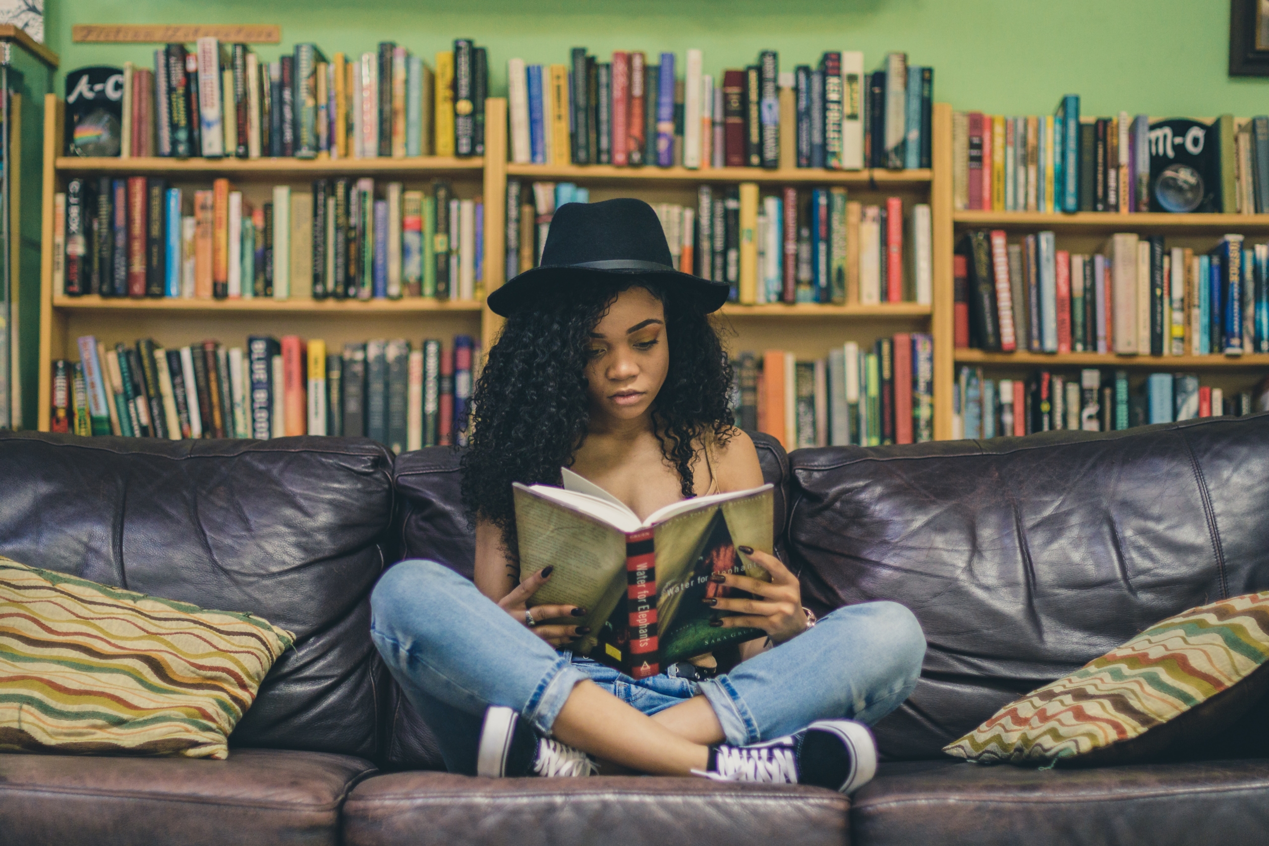 本棚の前のソファで本を読む女性