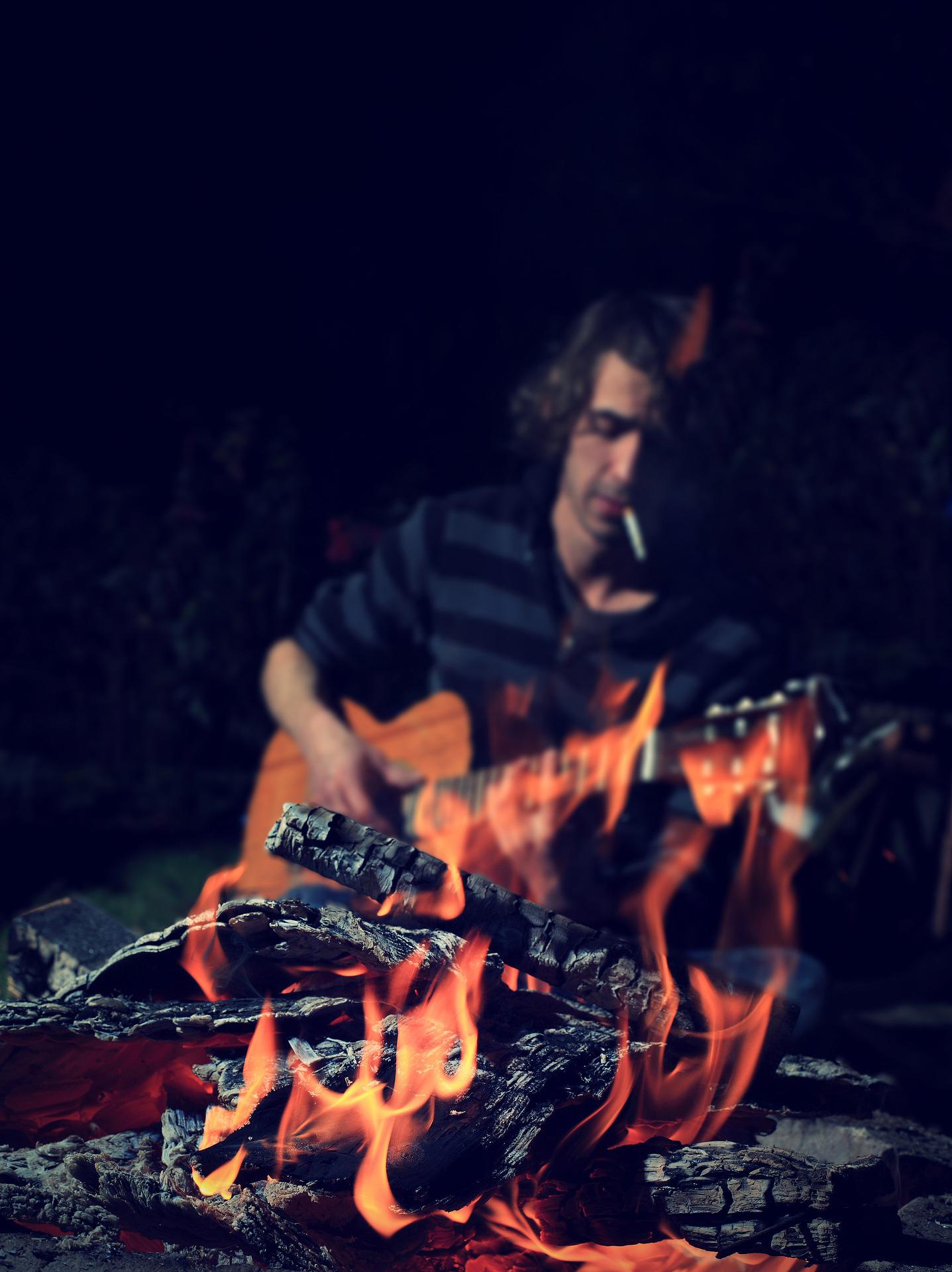 焚火の前でたばこをくわえながらギター