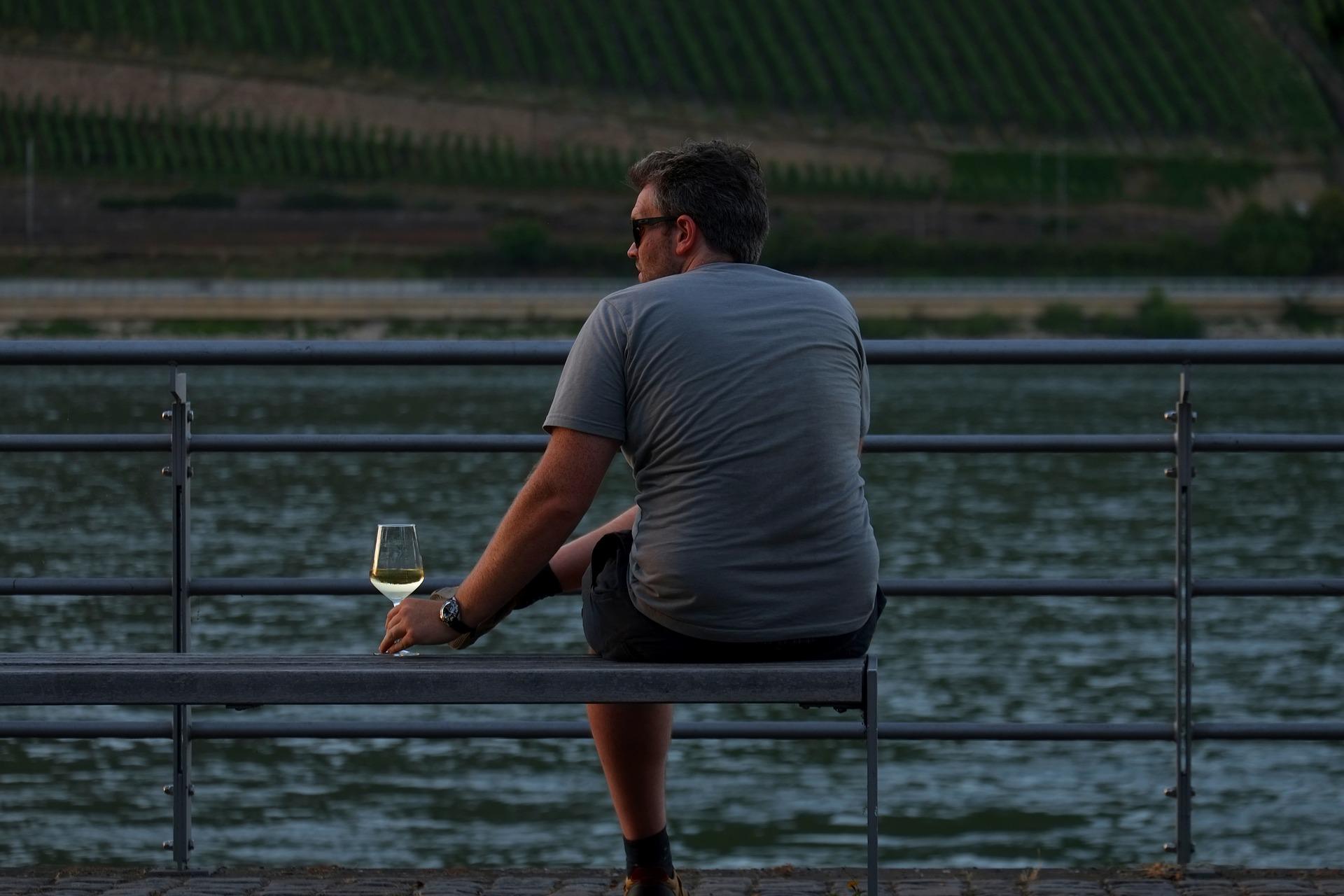 川辺のベンチでワインを飲む男性