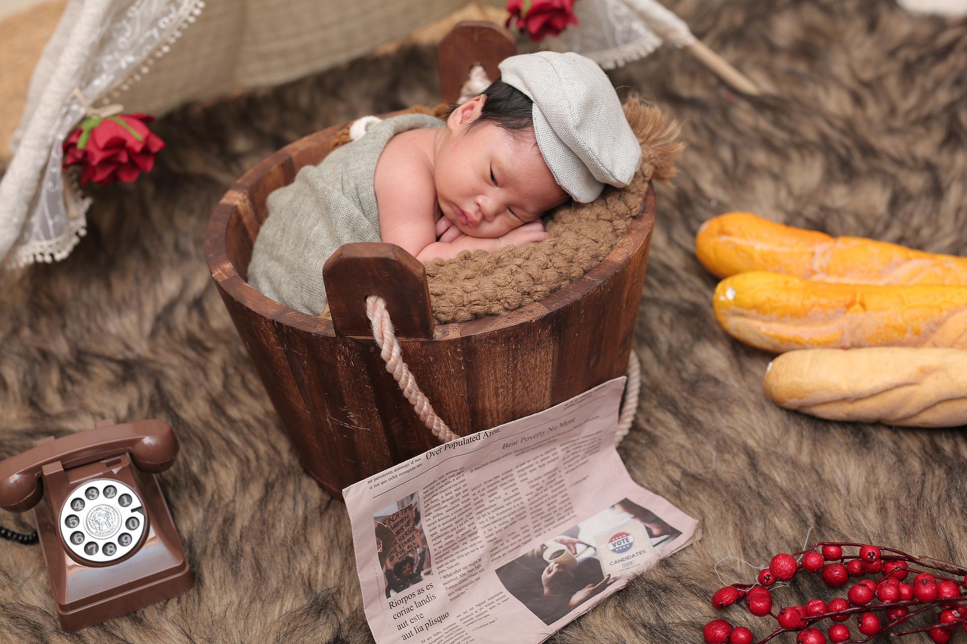 新聞が寄り掛かった木樽に入る赤ちゃん