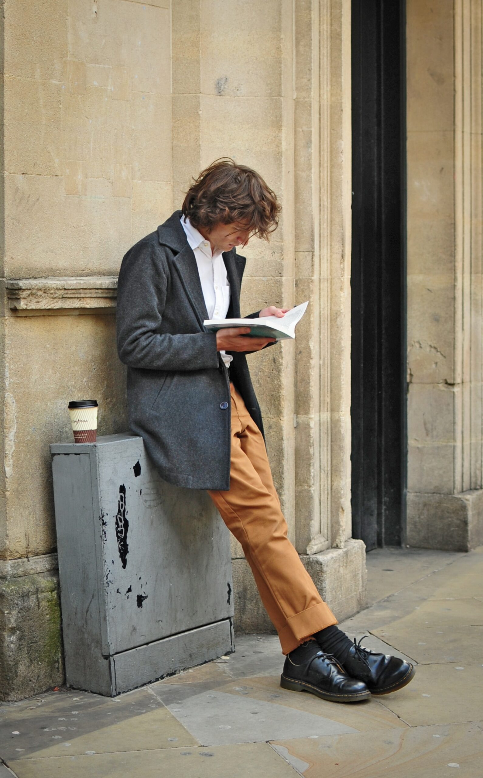 壁際にもたれて本を読む男性